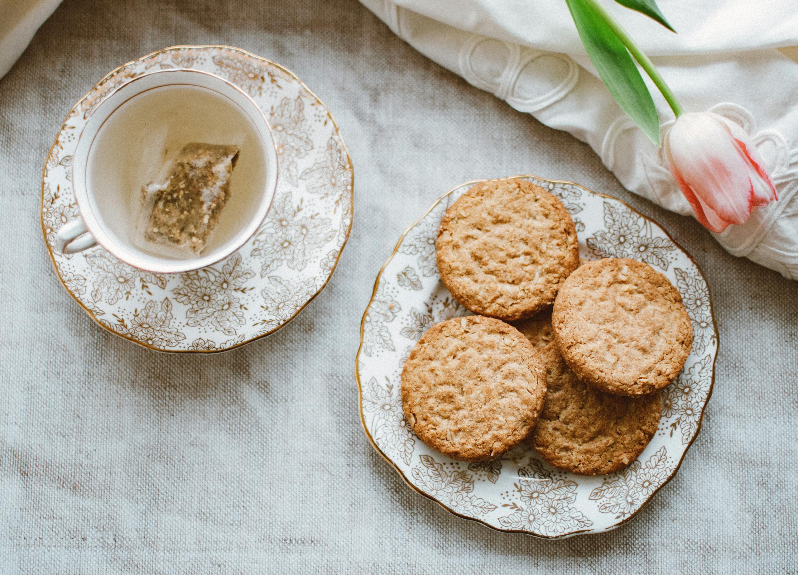 A charming morning tea setup with floral porcelain, biscuits, and tulip on a linen tablecloth.