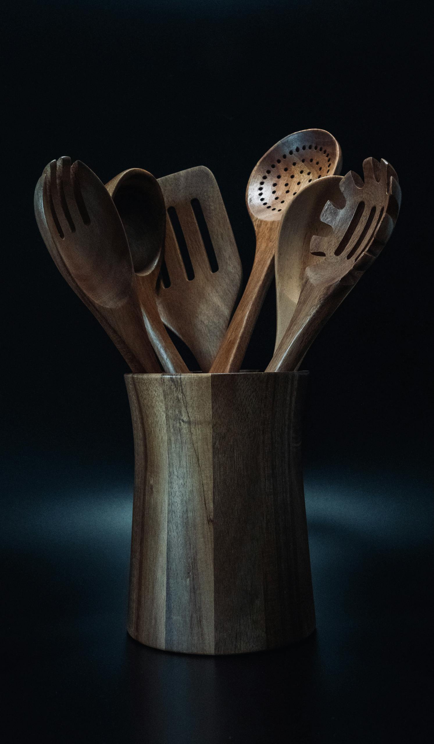 A collection of wooden kitchen utensils displayed in a stylish holder against a dark background.