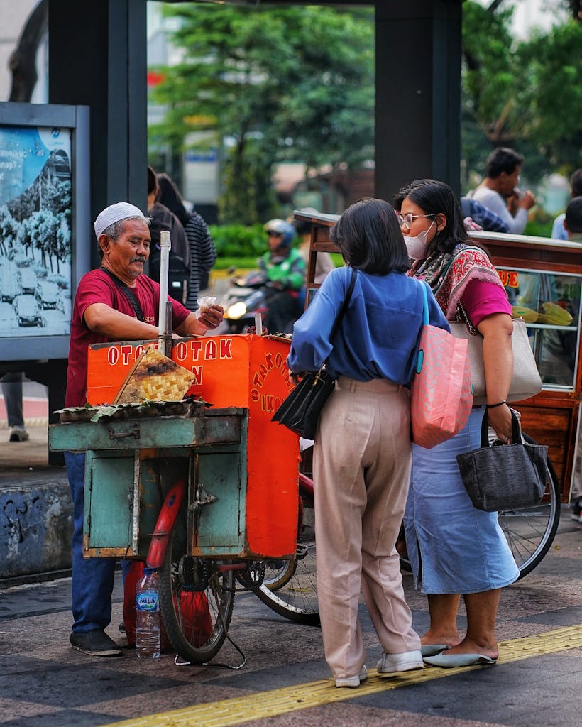 A street food vendor selling snacks to people on a busy street in Jakarta, Indonesia.