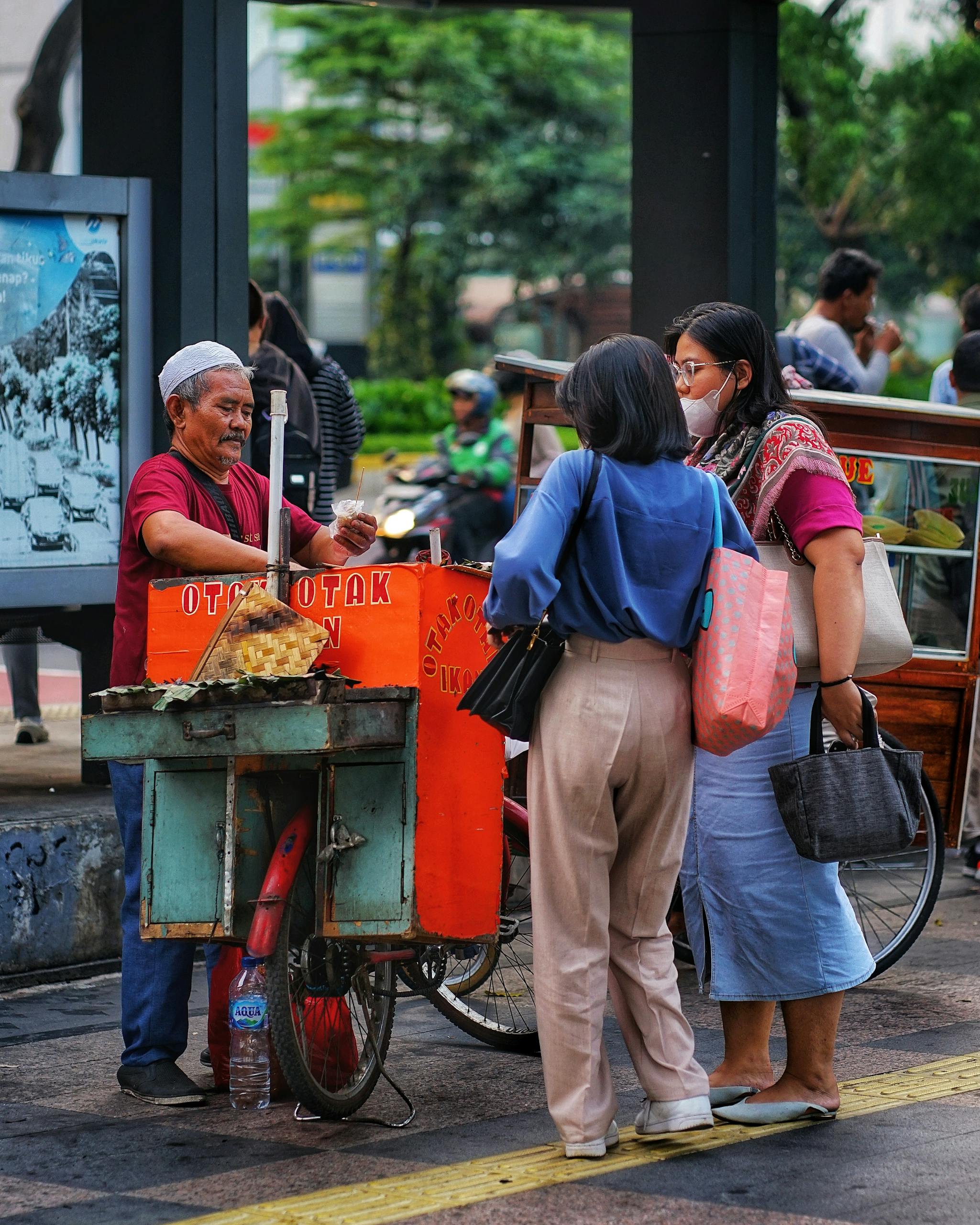 A street food vendor selling snacks to people on a busy street in Jakarta, Indonesia.