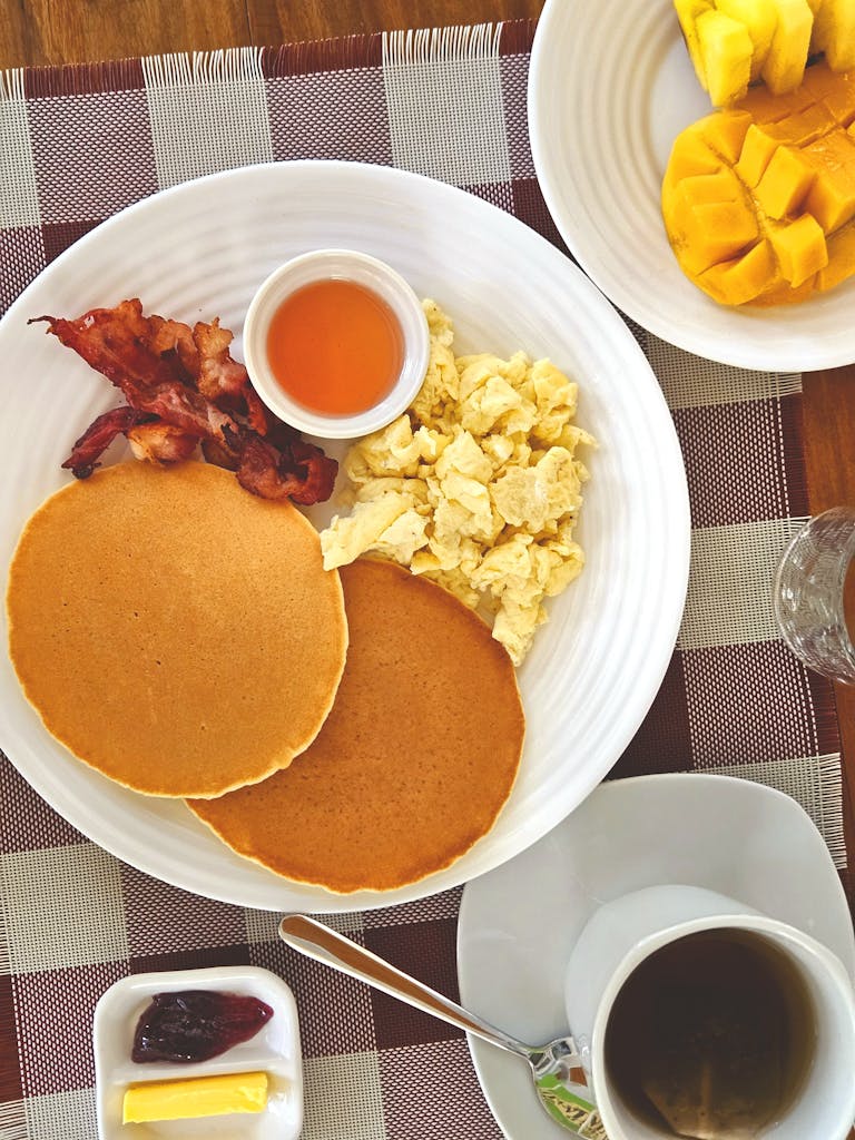 A vibrant tropical breakfast featuring pancakes, bacon, and fresh mangoes in a resort setting.