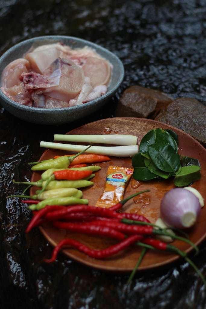 Assorted fresh vegetables and raw chicken for traditional Asian cooking in an outdoor setting.