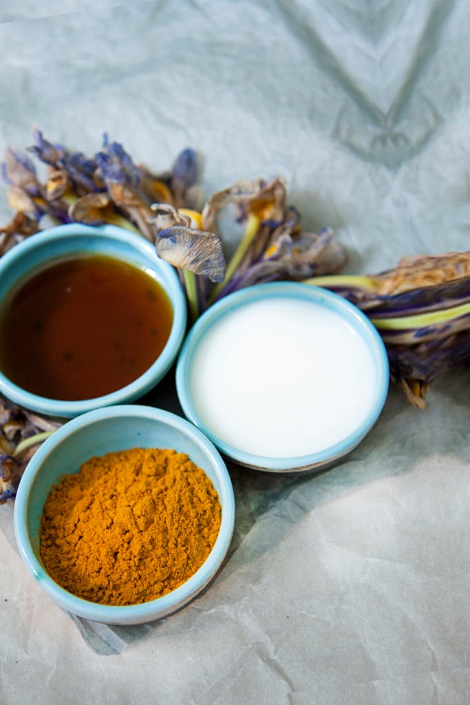 Bright culinary scene with turmeric, soy sauce, and milk flanked by dried flowers.