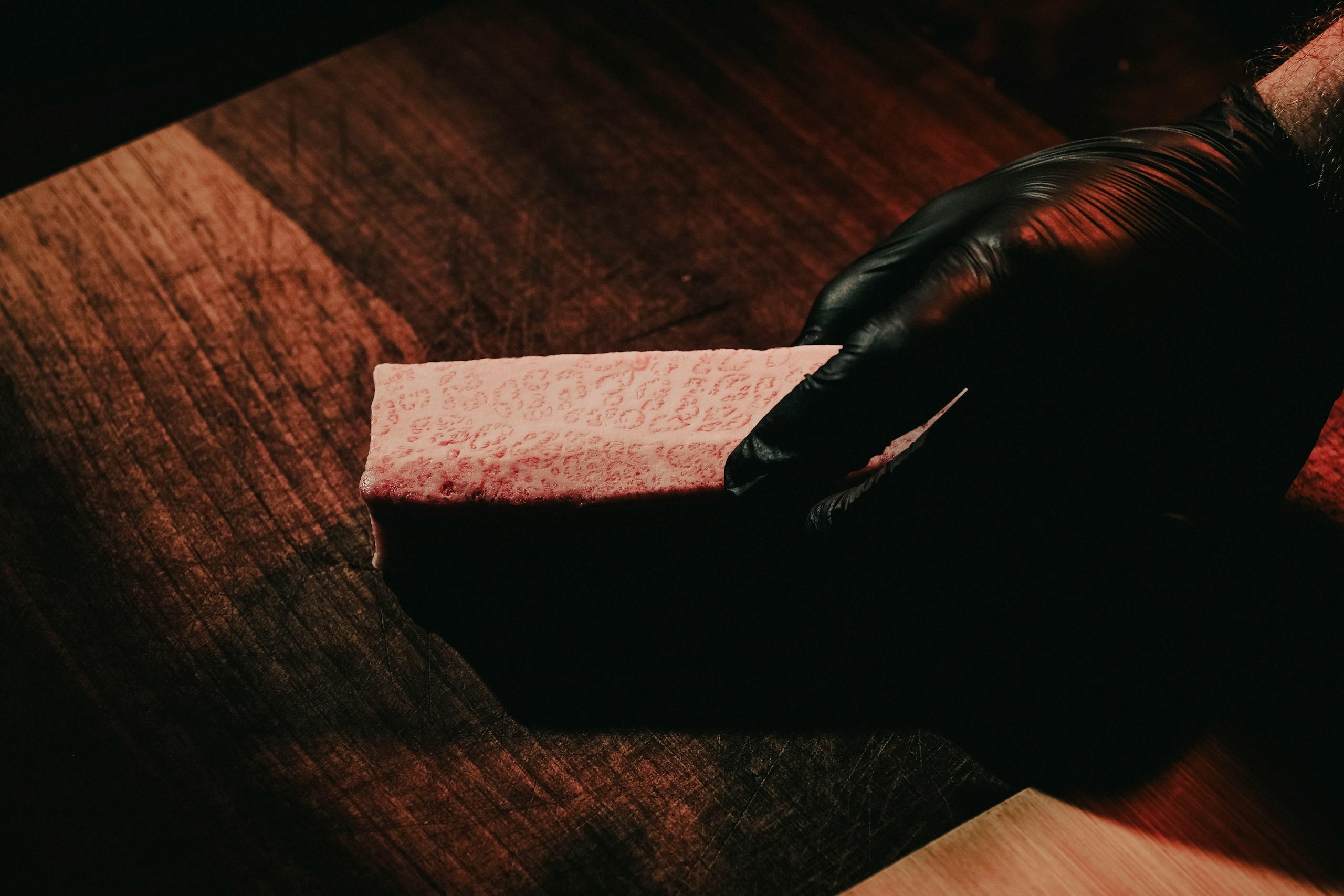Close-up of a raw Wagyu steak held by a gloved hand on a wooden surface.
