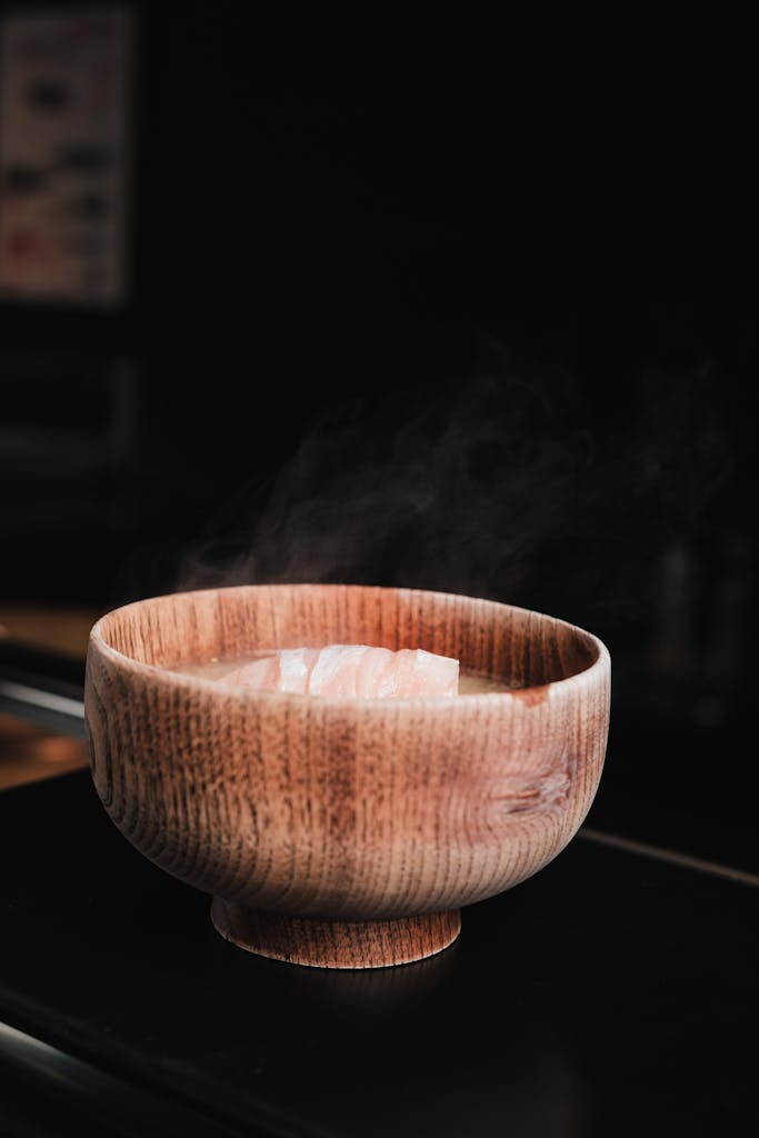 Close-up of a steaming bowl of traditional miso soup served in a wooden bowl.