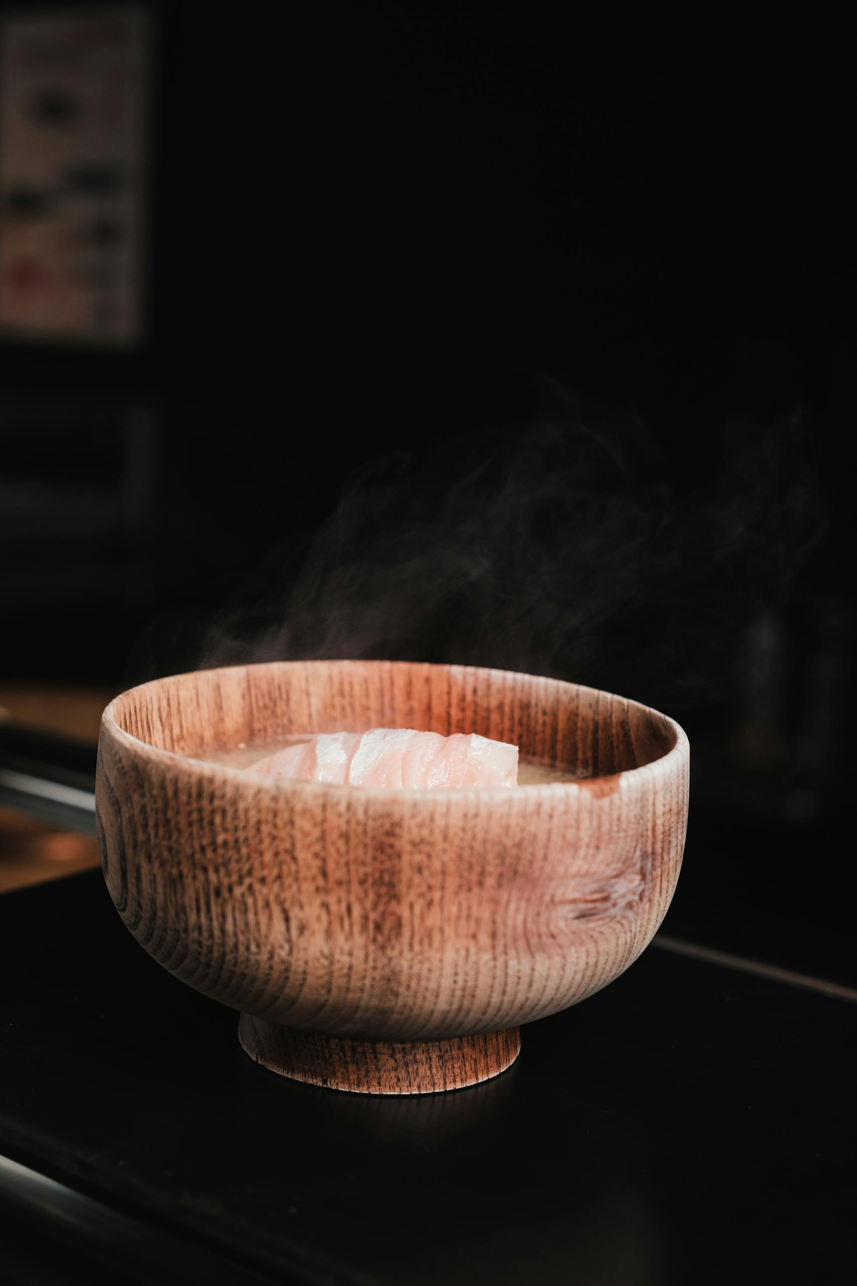 Close-up of a steaming bowl of traditional miso soup served in a wooden bowl.