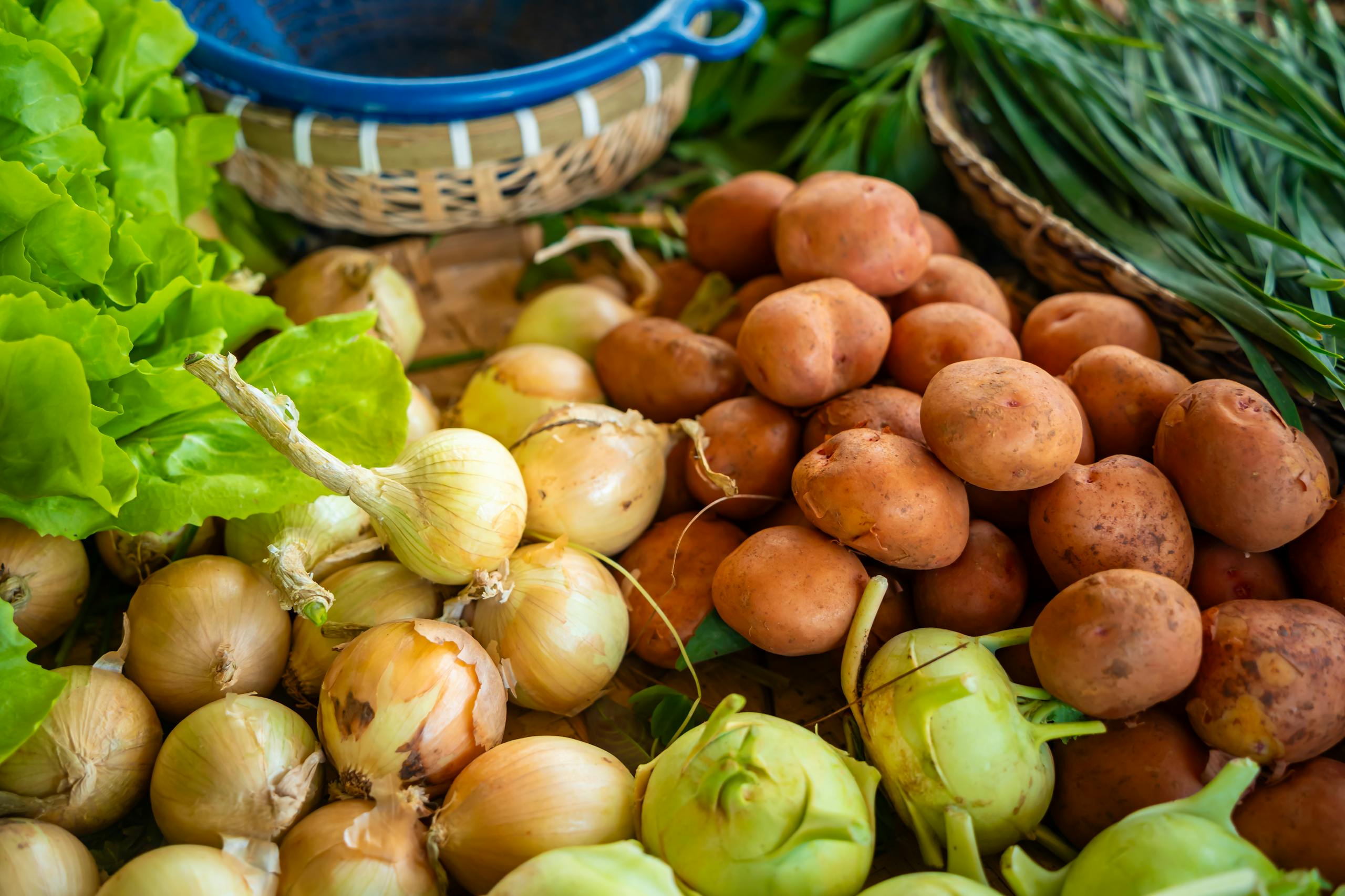Close-up of assorted fresh vegetables including onions, potatoes, and greens at a farmers market stall.