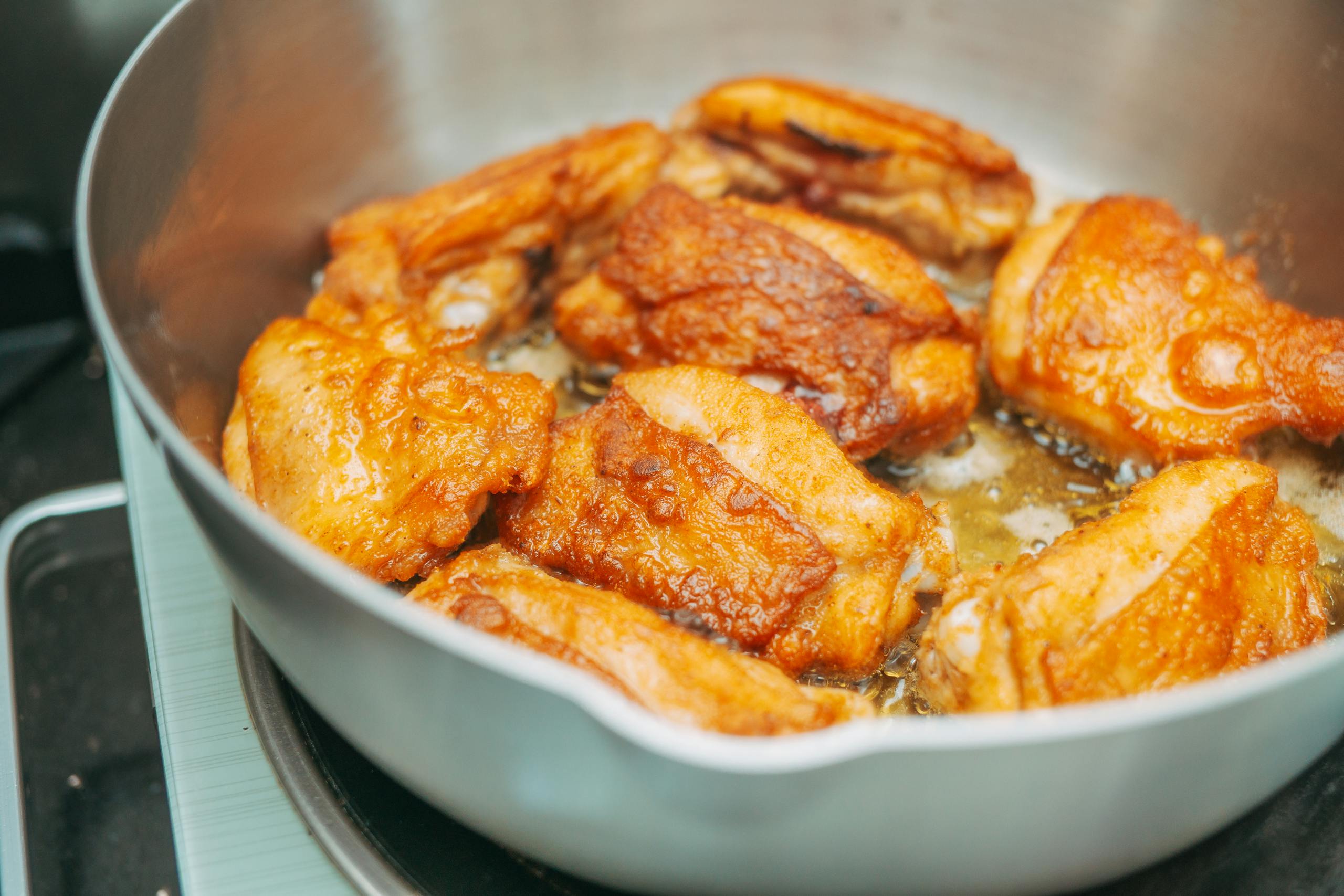 Close-up of crispy fried chicken thighs sizzling in a hot pan, perfect for meal inspiration.