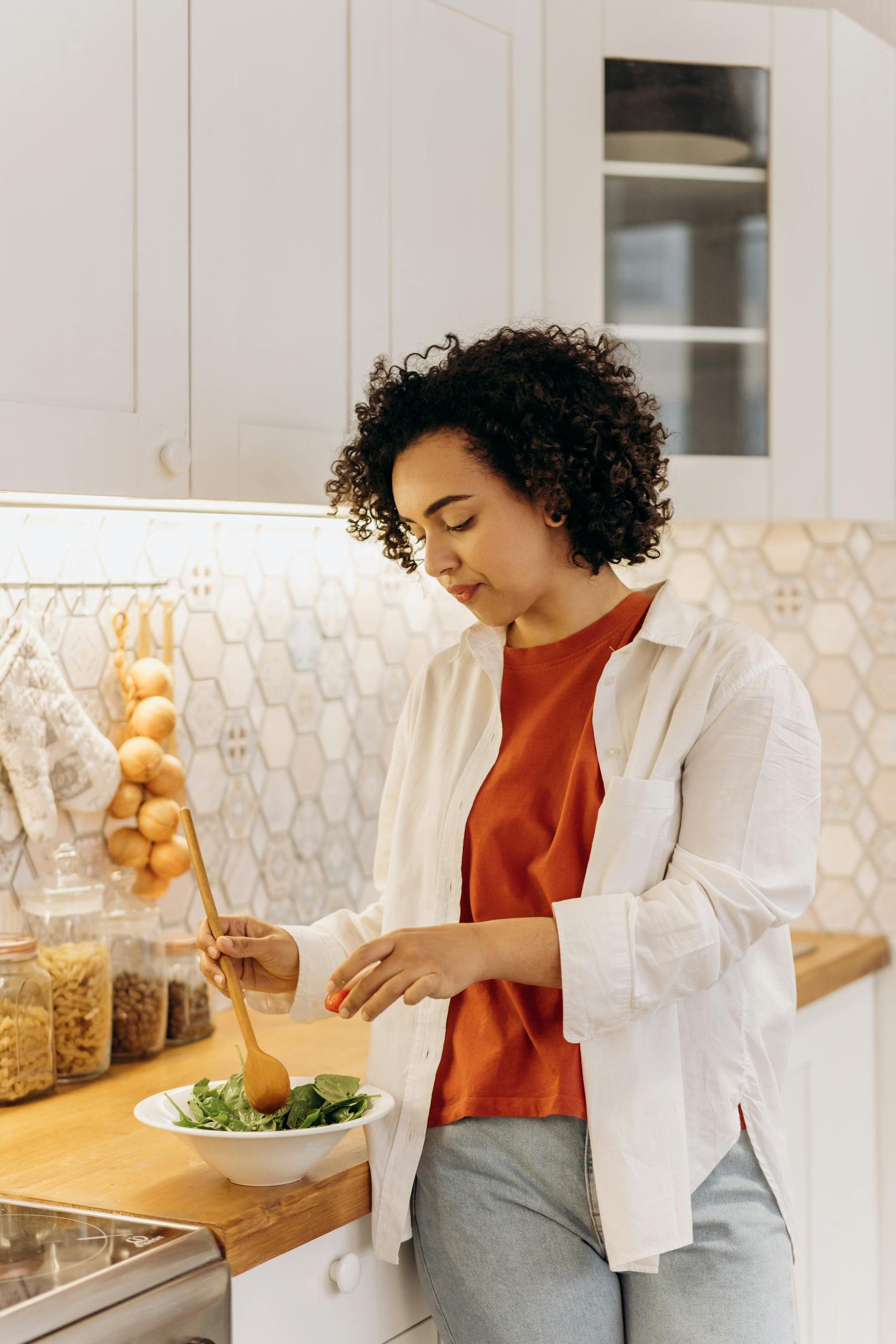 Curly-haired woman in a kitchen making a fresh salad, embracing a healthy lifestyle.