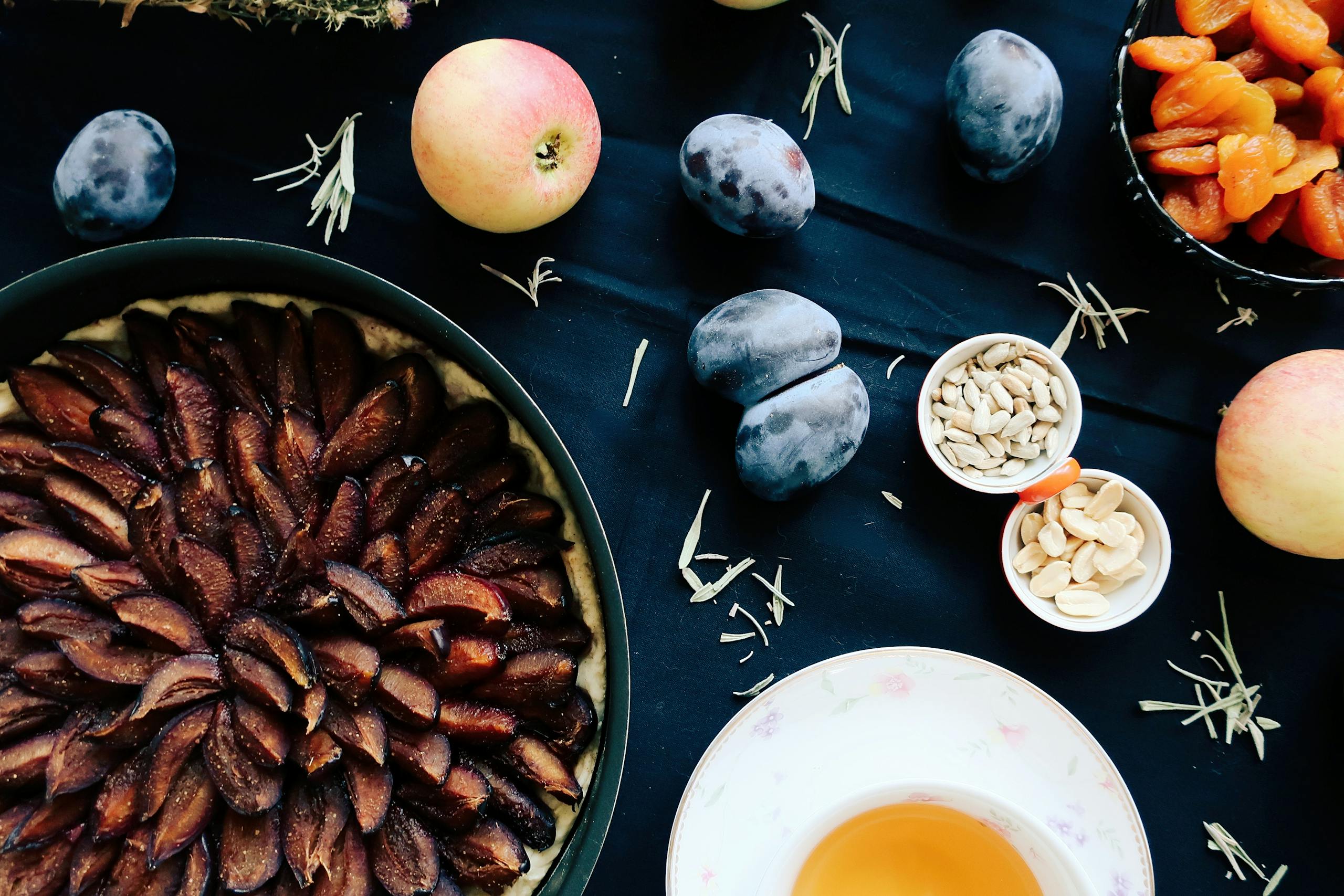 Delicious homemade plum tarte tatin surrounded by fresh fruits and nuts.