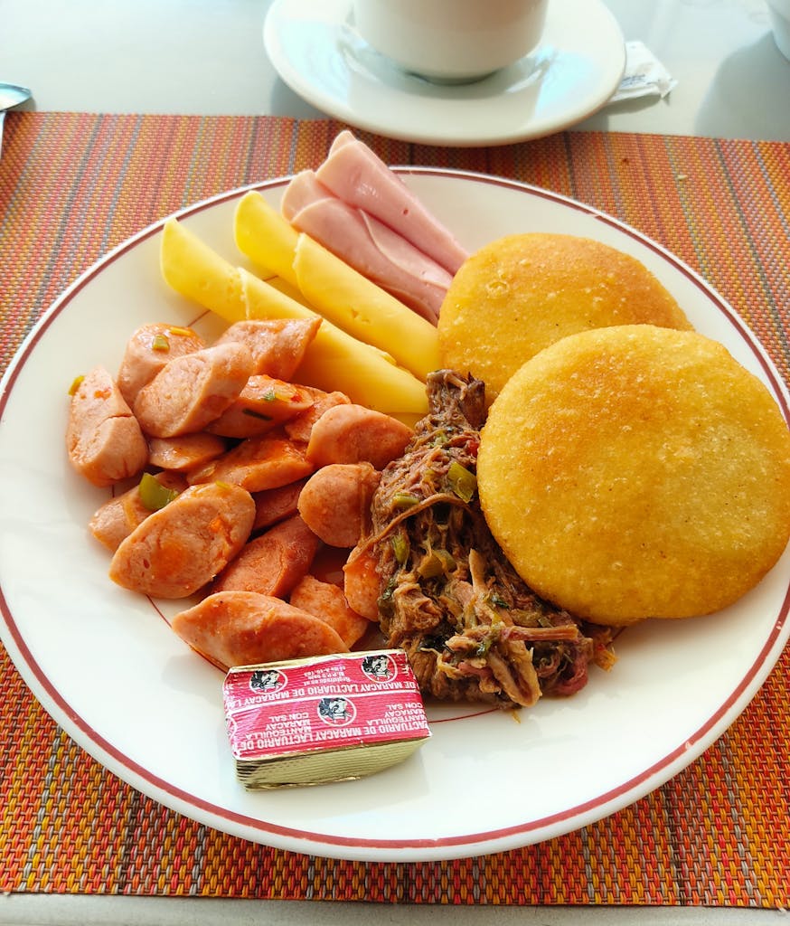 Delicious Venezuelan breakfast featuring arepas, sausages, cheese, and shredded beef.