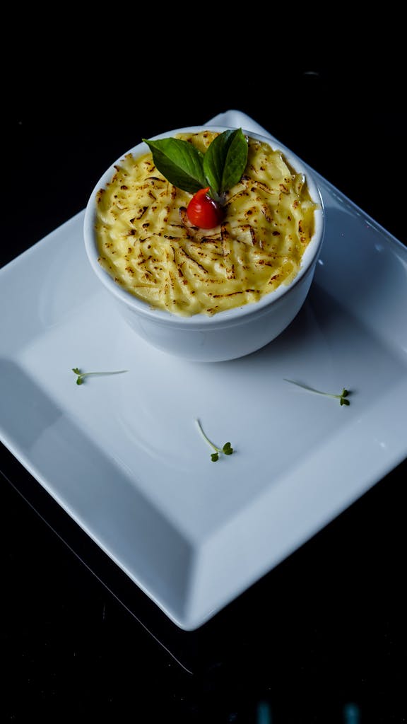 High-angle view of a gourmet mashed potato dish garnished with tomato and basil in a white ceramic bowl.