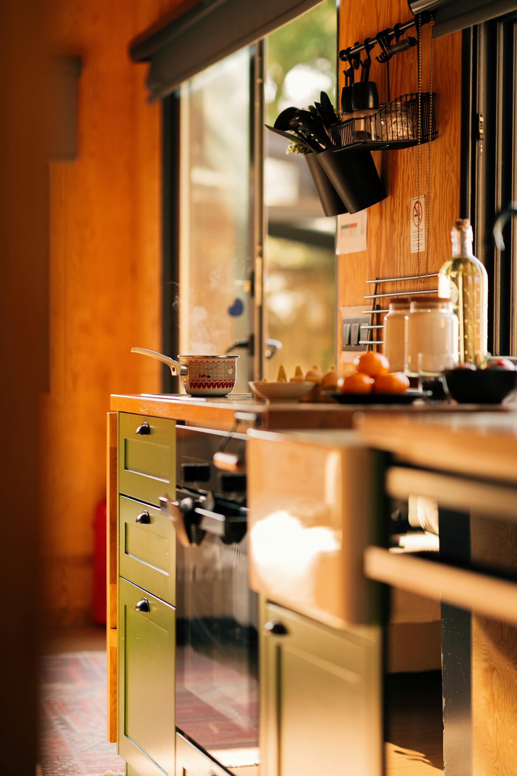 Sunlit modern kitchen interior with green cabinets and cooking essentials.