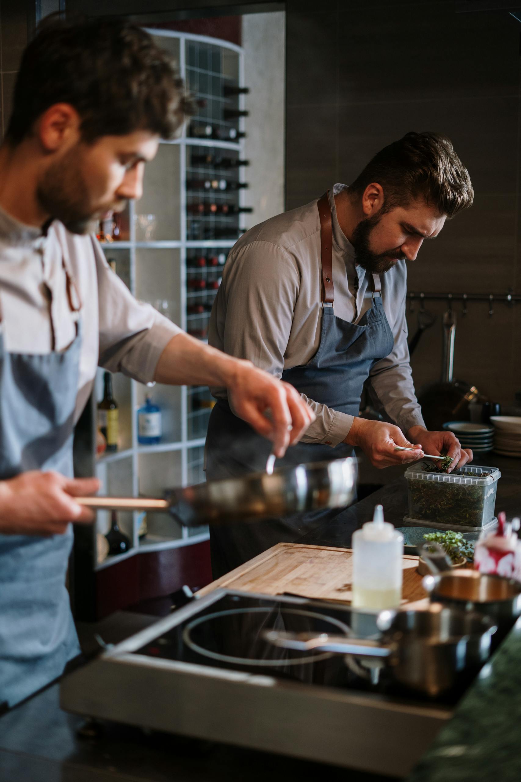 Two male chefs preparing dishes in a professional open kitchen setting.