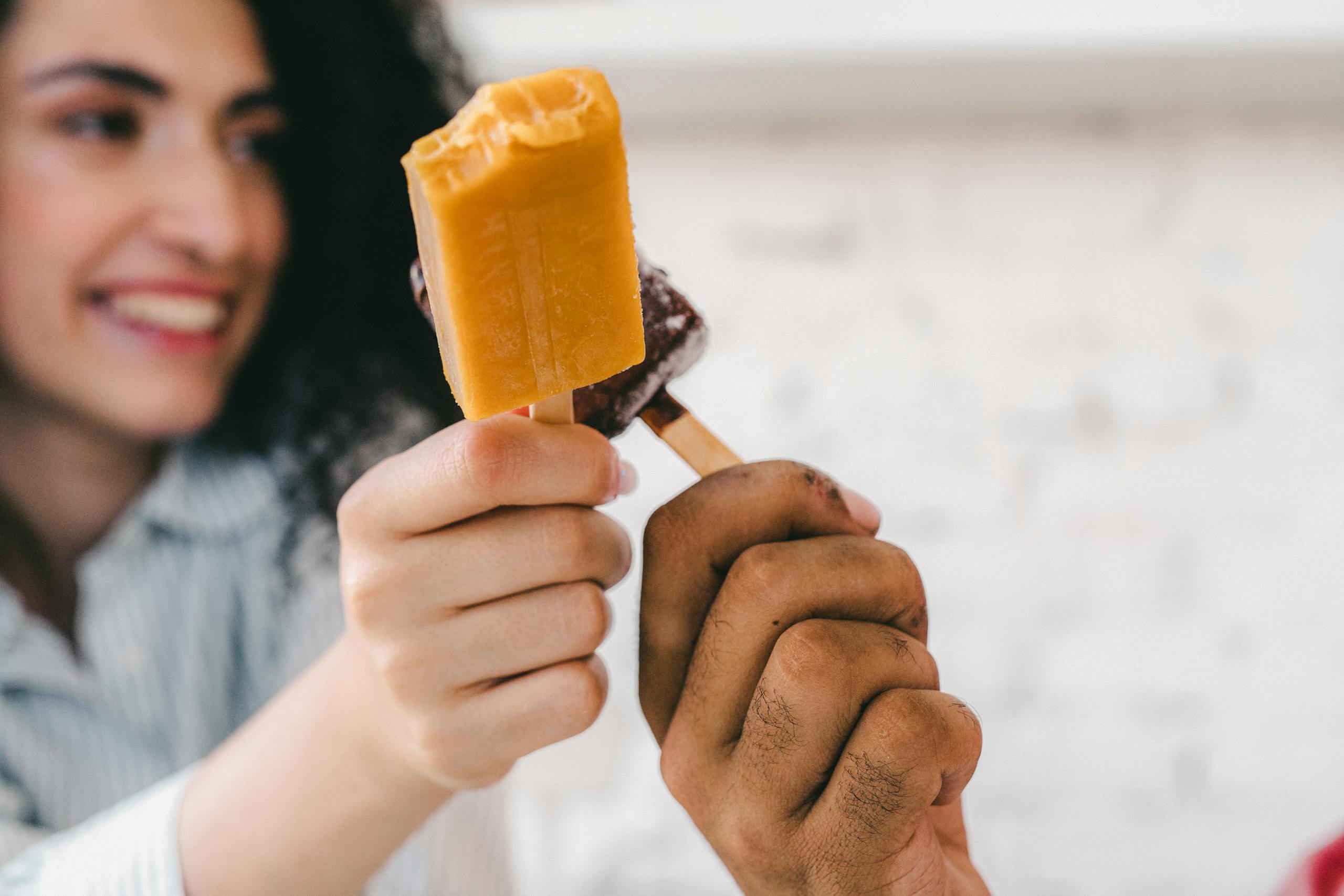 Two people sharing popsicles in a joyful moment indoors.